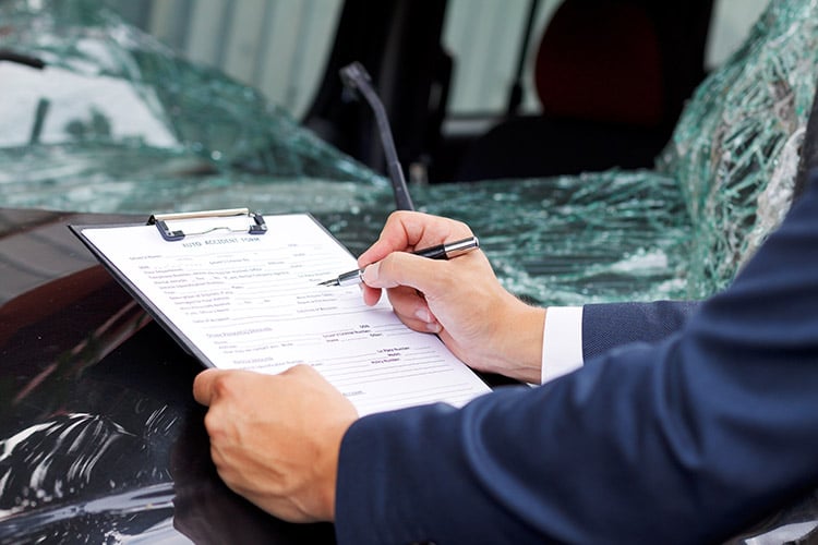 Insurance loss adjuster inspecting damaged vehicle shattered glass in background