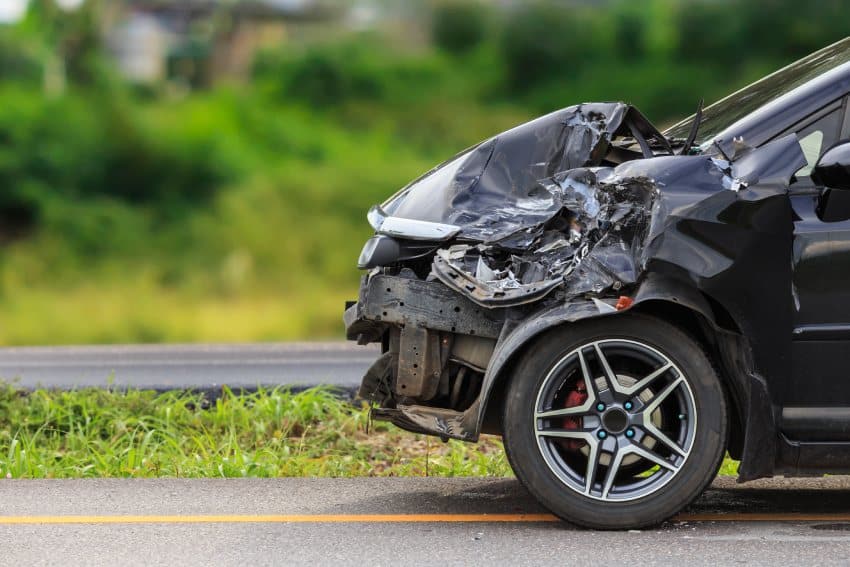 Black car at roadside with significant front damage after crash with another vehicle