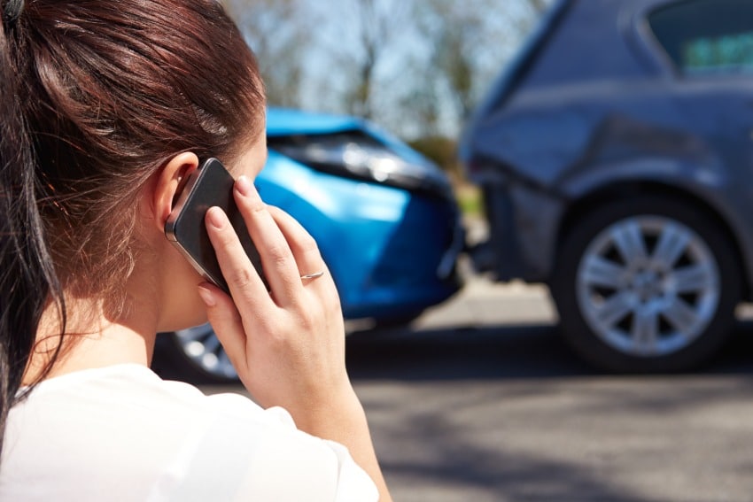 Female driver making call on cellphone after car crash between blue and dark gray cars