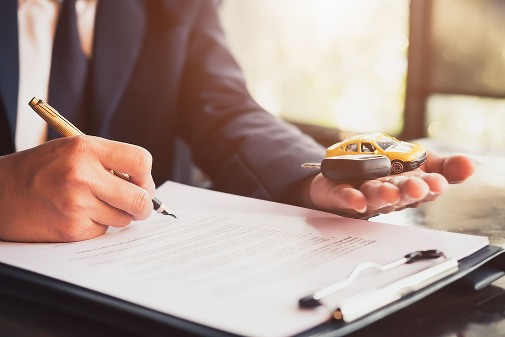Male insurance agent signing document and holding toy car and key in palm of his left hand
