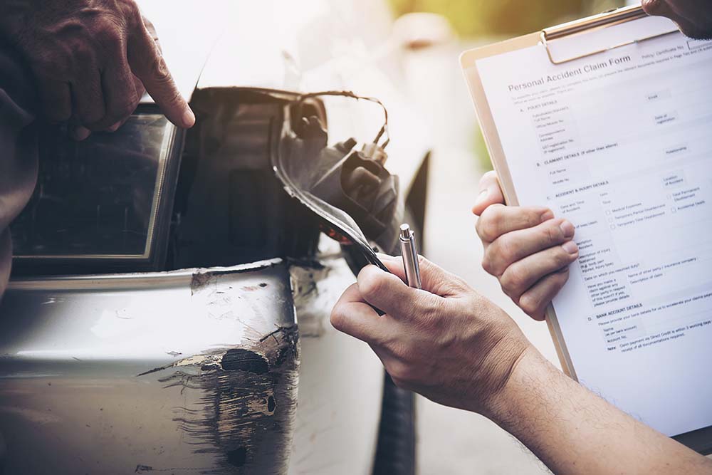 Insurance agent and car owner completing accident report and inspecting damage after a car crash