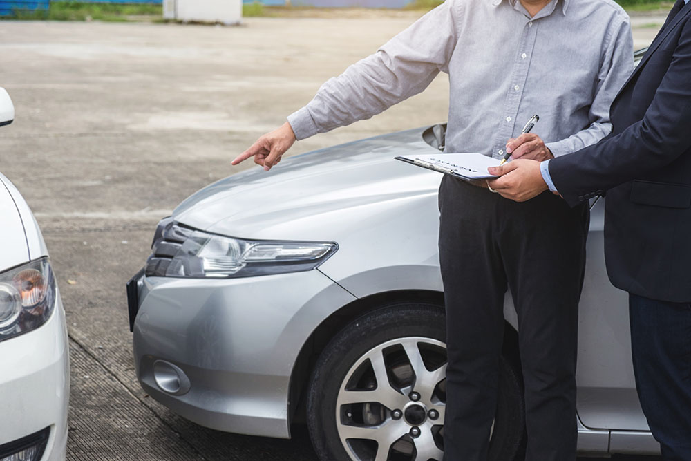 Two male insurance agents reading clipboard report and discussing car crash