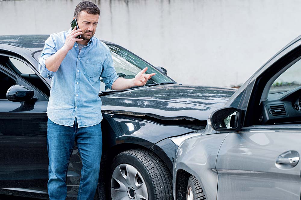 Stressed man in denim shirt talking on phone and gesturing after front end collision