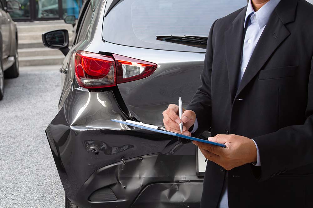 Insurance agent checking and changing crash report in front of vehicle