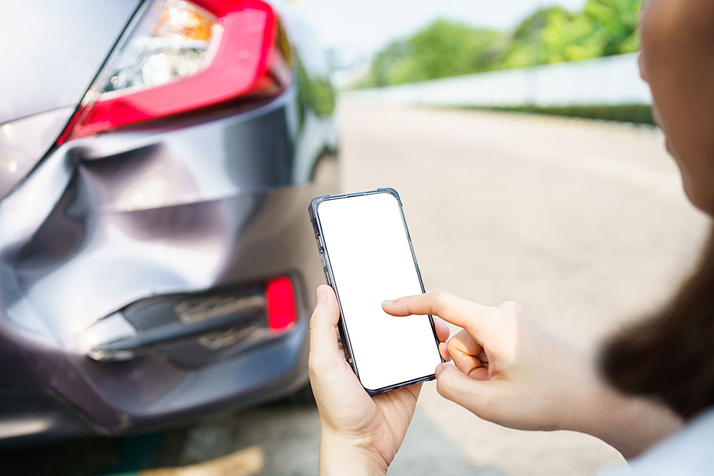 Closeup of woman taking picture of rear car damage on cellphone