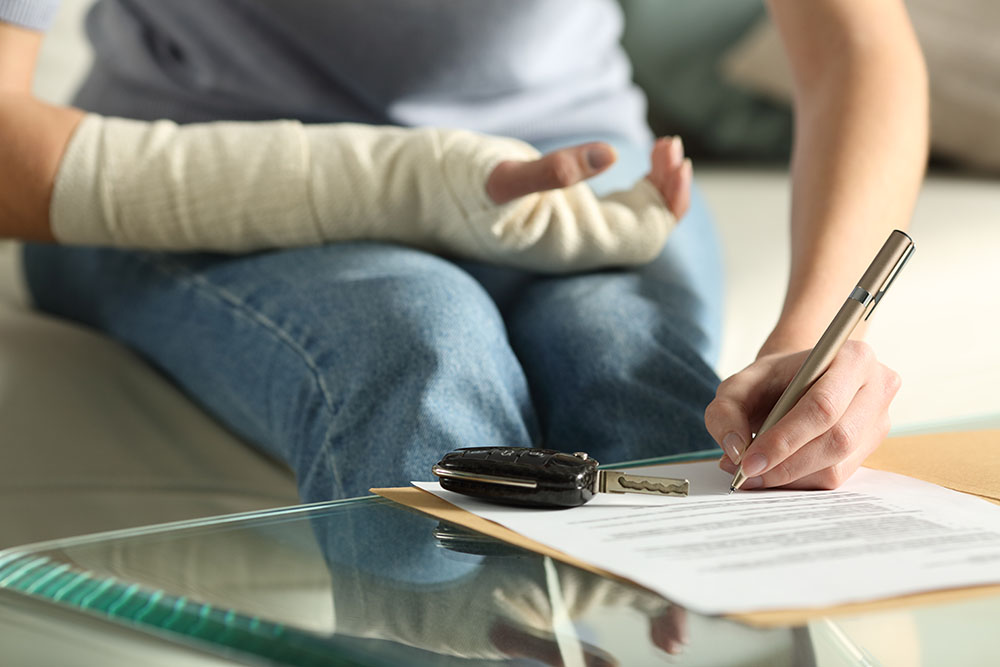 Close up of a woman with broken wrist completing an accident claims form with car keys at side