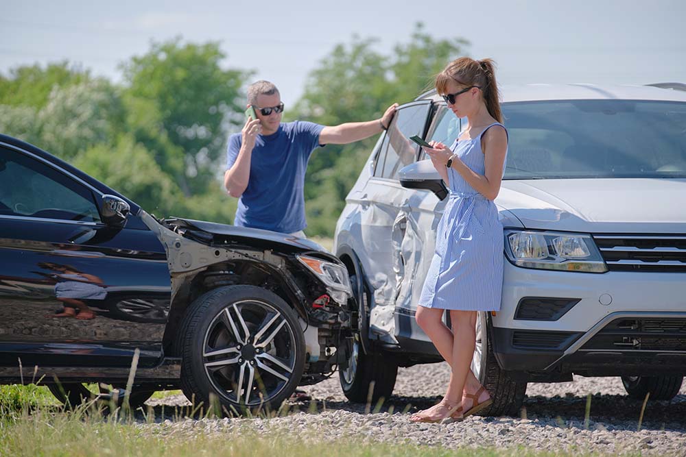 Young woman texting after a sideswipe car accident on sunny day between male and female drivers