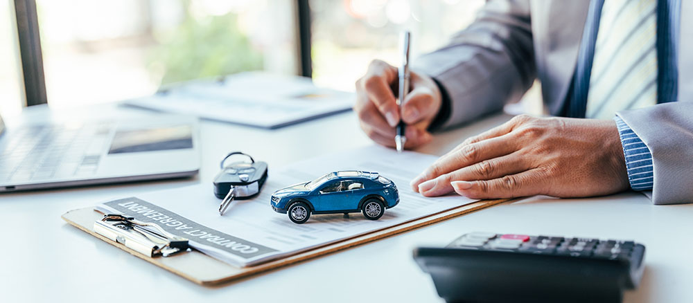 Close up of driver signing a car accident insurance document with keys and toy car in foreground