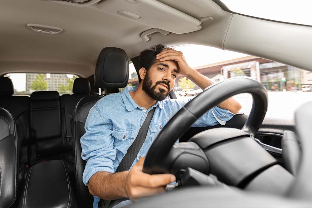 A man sitting in his car and holding his head after an accident