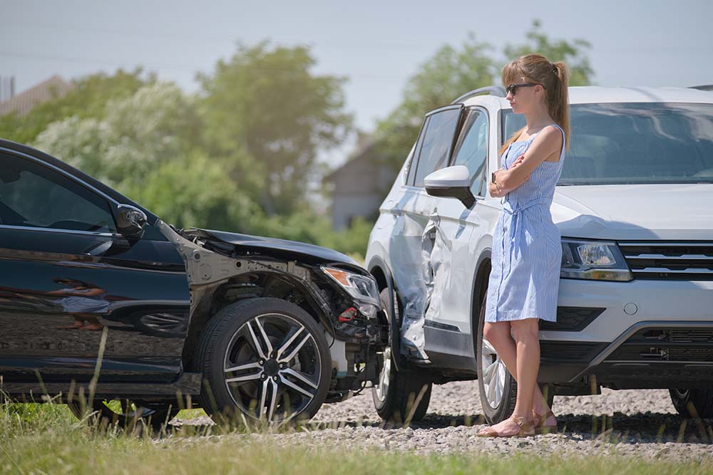 A woman standing in front of a car accident with a sedan and an SUV