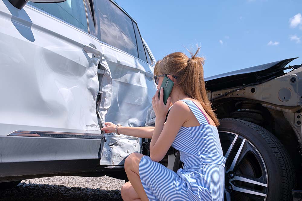 A woman on the phone looking at a crashed car