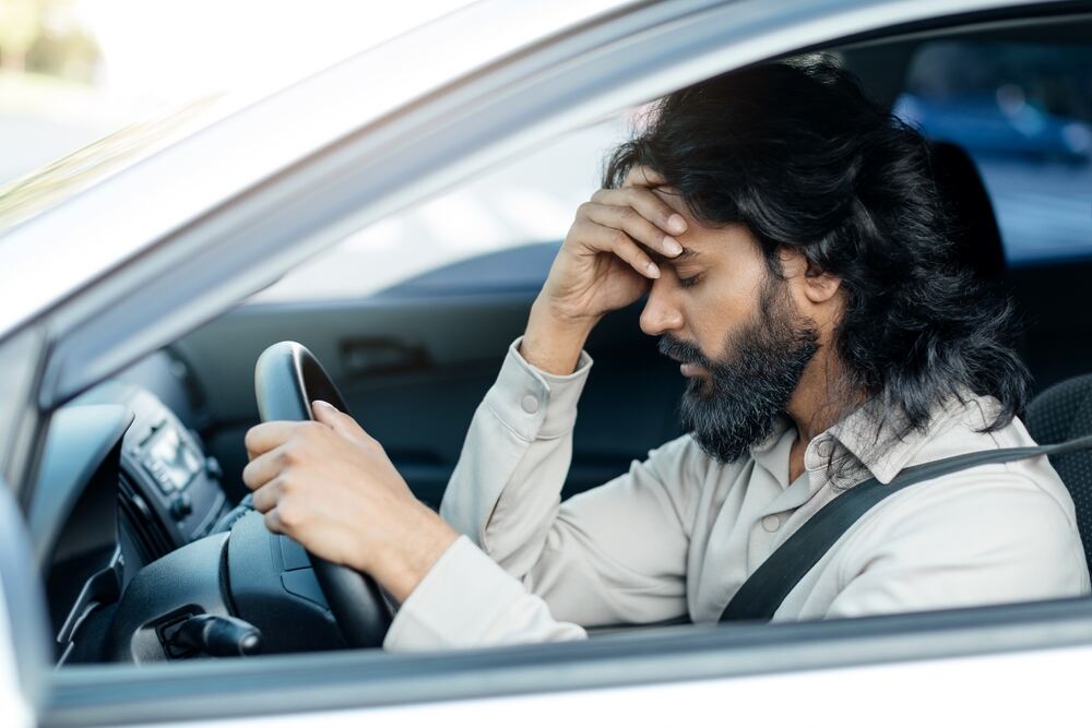 An arab-descent male holding his brow in upset in the front seat after an accident. 