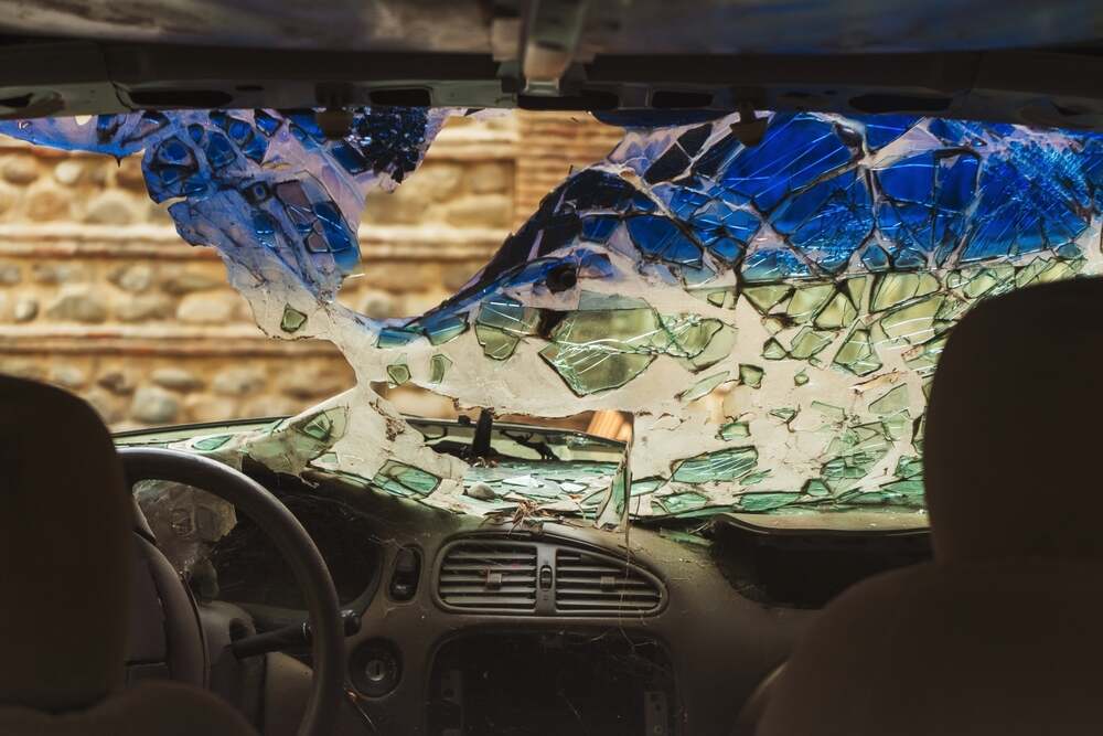 A photo from inside a car after an accident; the front windshield is buckled and broken.  